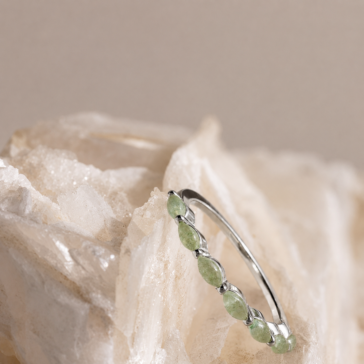Silver ring with green gemstones on a textured beige background